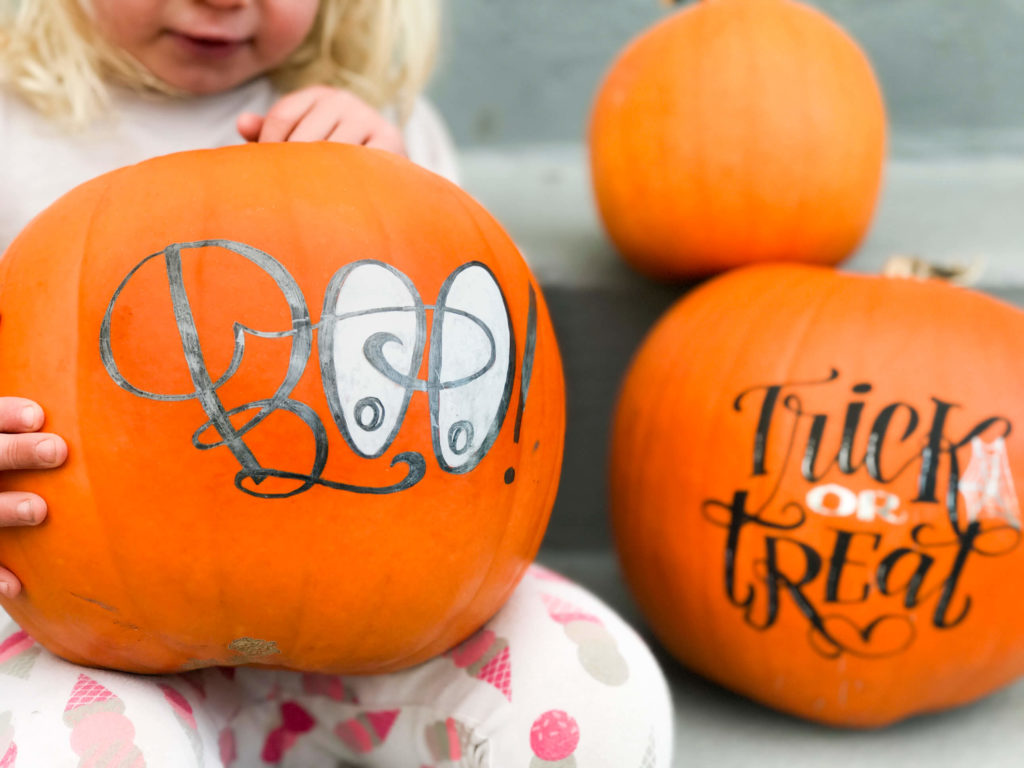 Little girl holding hand lettered pumpkin